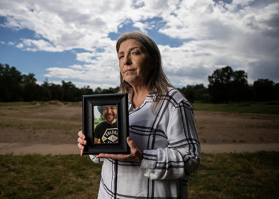 Jeanelle Couch holds framed photo of her son, David Couch, who was killed in a shooting involving a California Highway Patrol officer. She is standing in Cascade Park in Redding with a sky full of clouds and open space behind her. — Larry Valenzuela // CalMatters