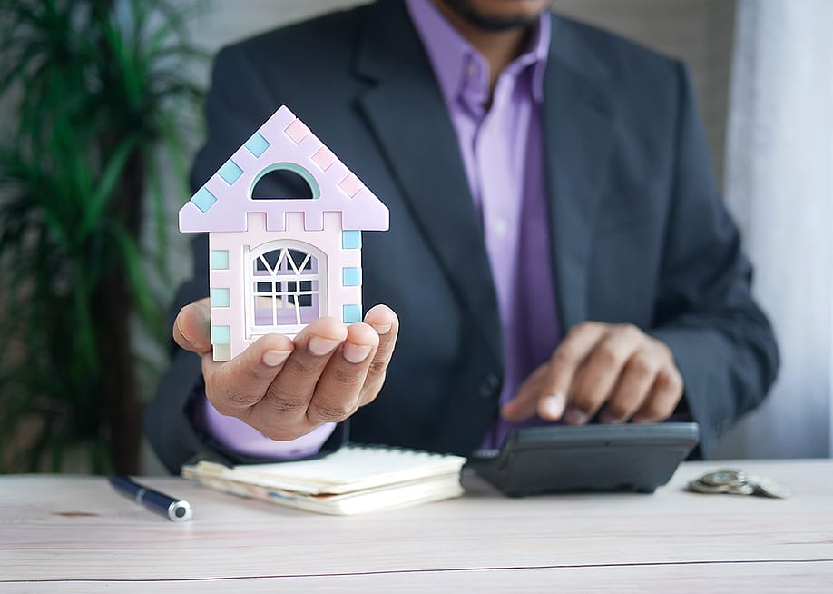 A finance professional holding a small figure of a house as a concept of investing in real estate. — Towfiqu ahamed barbhuiya // Shutterstock