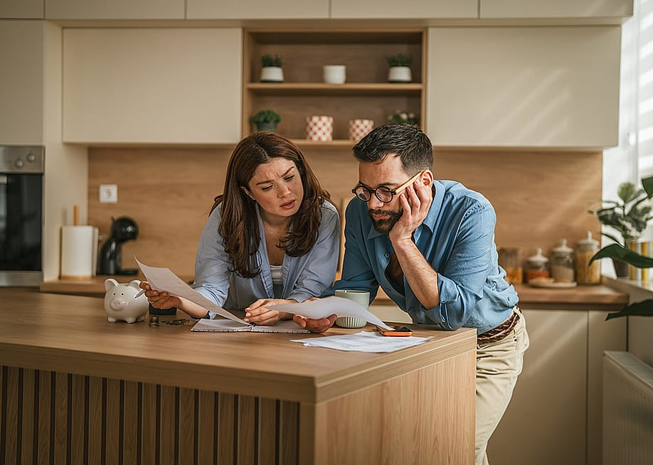 A couple reviewing bills and documents from their household finances at their home's kitchen. — Miljan Zivkovic // Shutterstock