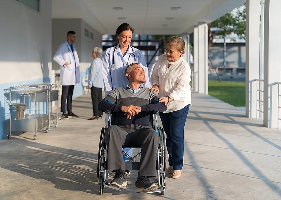 A female doctor assisting her patient in pushing his wheelchair along with a companion. — Naypong Studio // Shutterstock