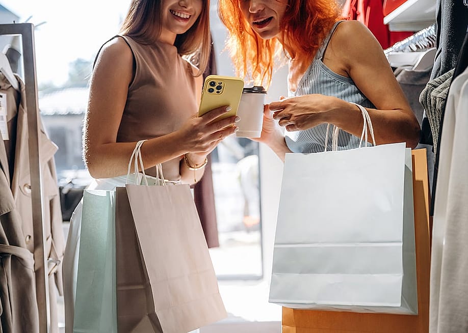 Two friends checking items' information from a smartphone after shopping clothes in a store. — Standret // Shutterstoc
