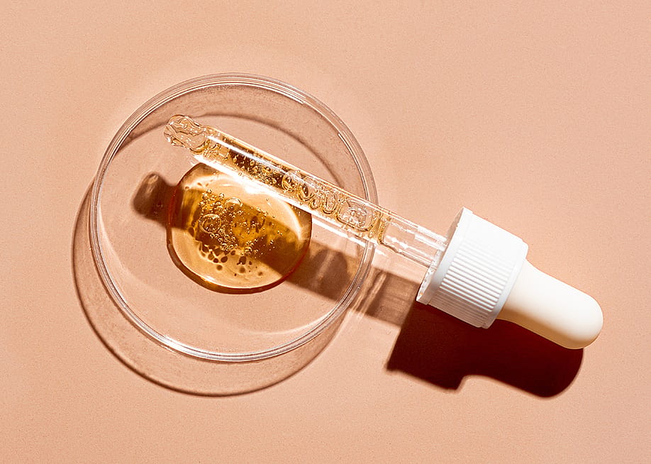 A dropper pipette and a petri dish with drops of oil or retinol gel on a beige nude background. — Oksana Mizina // Shutterstock