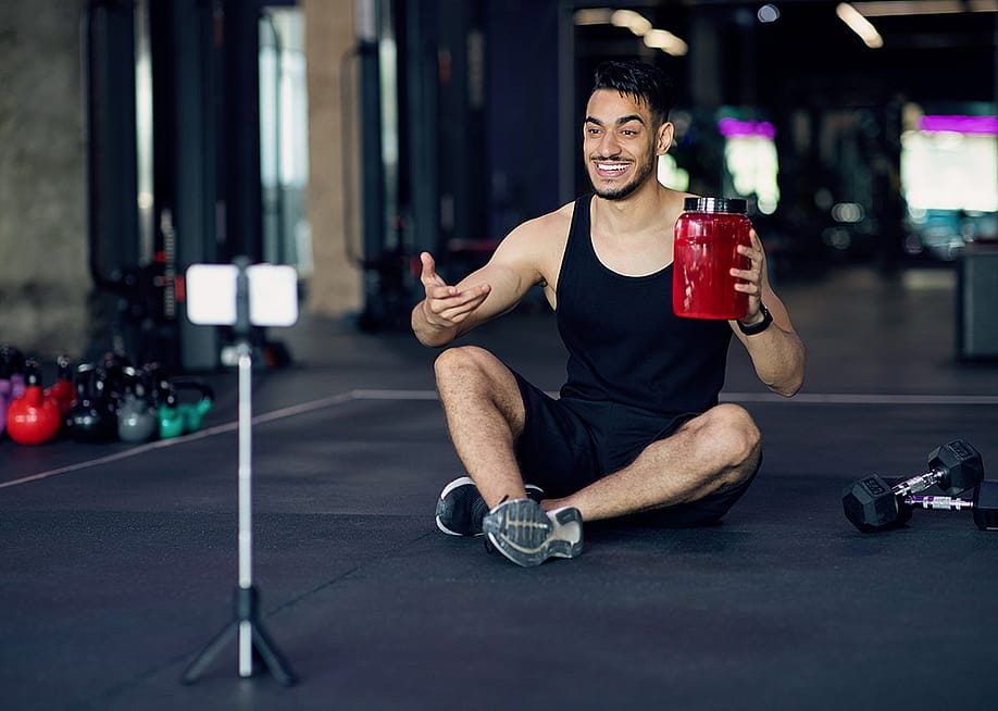 A fitness blogger recording himself from his smartphone at a gym for a sport wellness video. — Prostock-studio // Shutterstock
