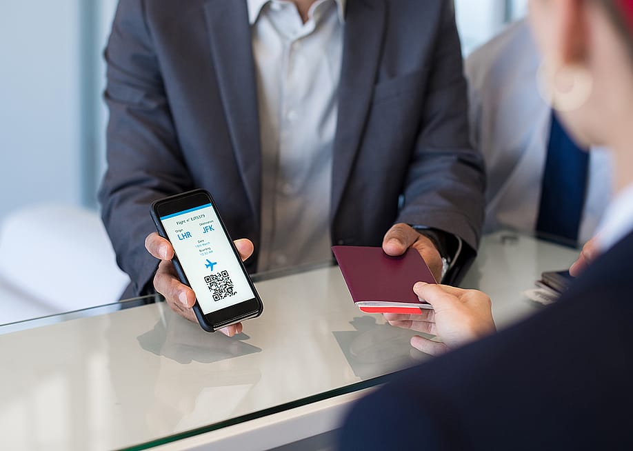 A businessman showing passport and flight ticket using his smartphone at airport check-in. — Ground Picture // Shutterstock
