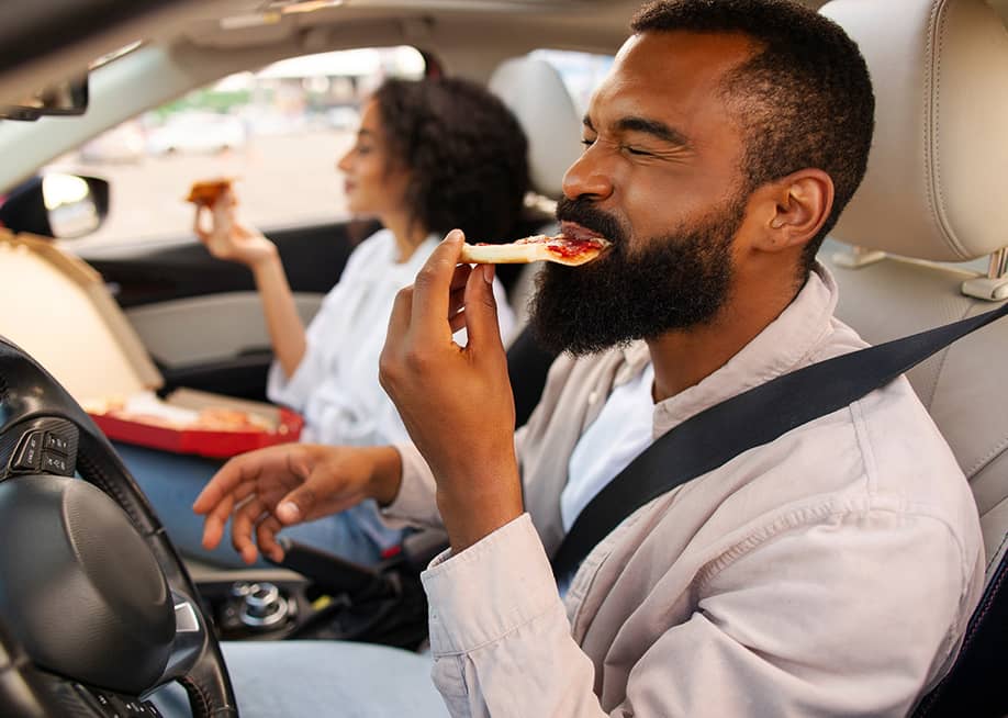 A couple eating pizza in the car during a road trip. — fast-stock // Shutterstock