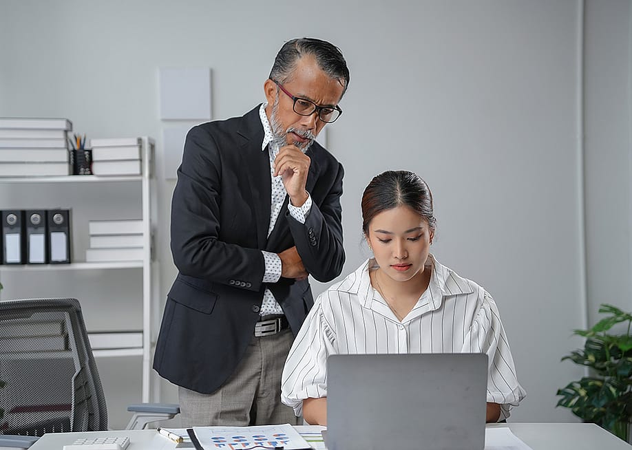 A manager standing behind an employee while checking her work report's progress. — Amnaj Khetsamtip // Shutterstock