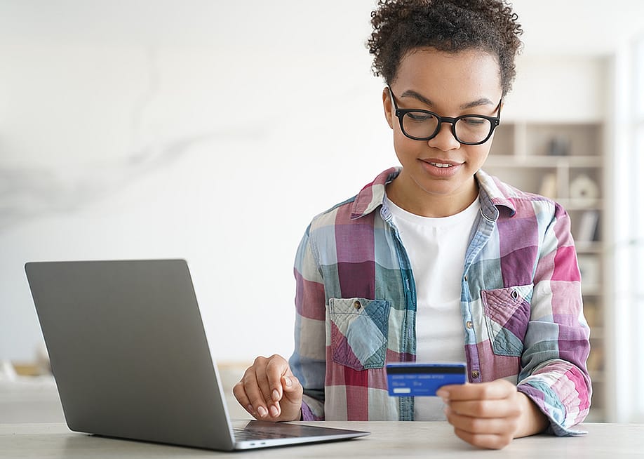 A teenager holding a credit card while shopping online from a laptop. — vk_st // Shutterstock