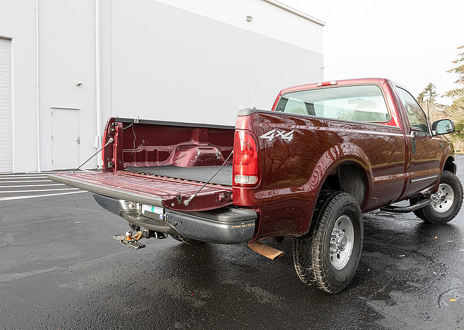 A burgundy 2000 Ford F-250 Super Duty pickup truck parked in an outdoor garage with its tailgate open. — Hrach Hovhannisyan // Shutterstock