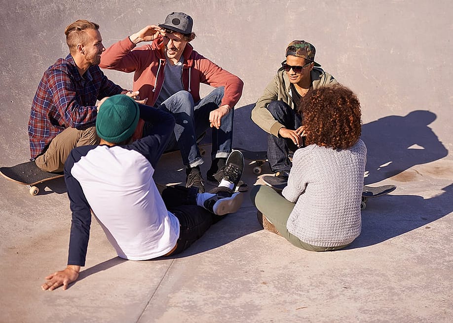 A group of adult skaters hanging out under the sun in a skate park. — PeopleImages // Shutterstock