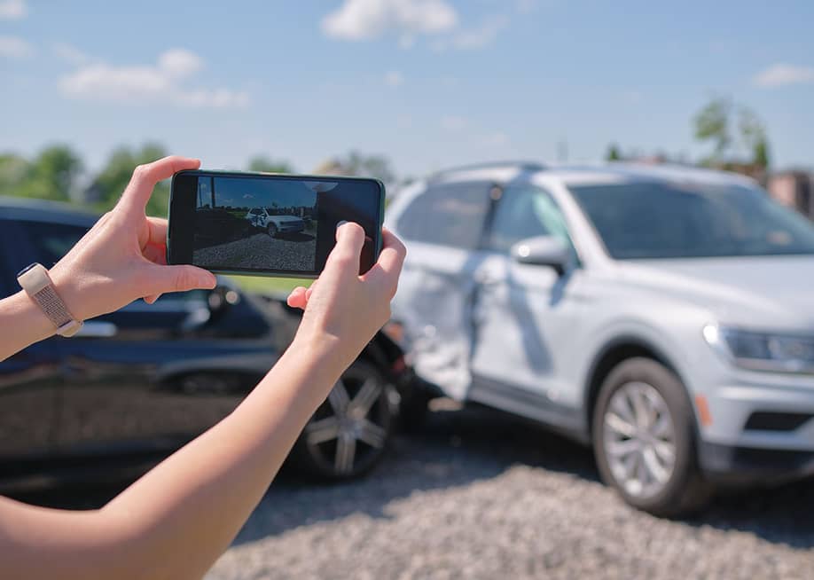 A driver taking a photo of their car's damage after an accident. — Bilanol // Shutterstock