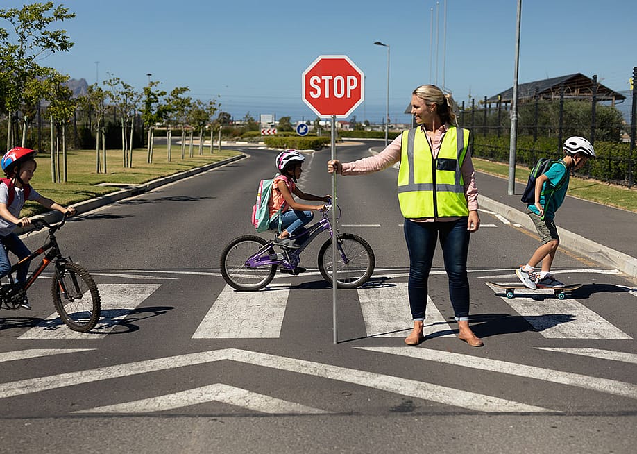 A female traffic enforcer helping school children riding bicycles cross the road. — wavebreakmedia // Shutterstock