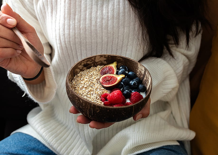 A woman holding healthy breakfast smoothie bowl with granola oats, fresh berries and figs. — Daniel Hoz // Shutterstock