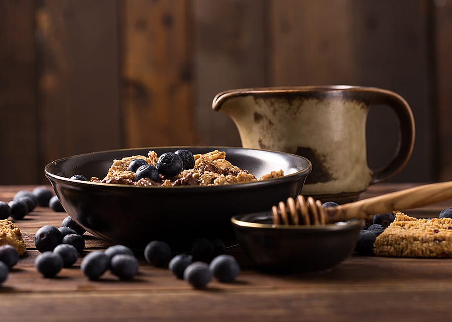 A muesli bowl with blueberries and honey placed in a table. — peterzsuzsa // Shutterstock