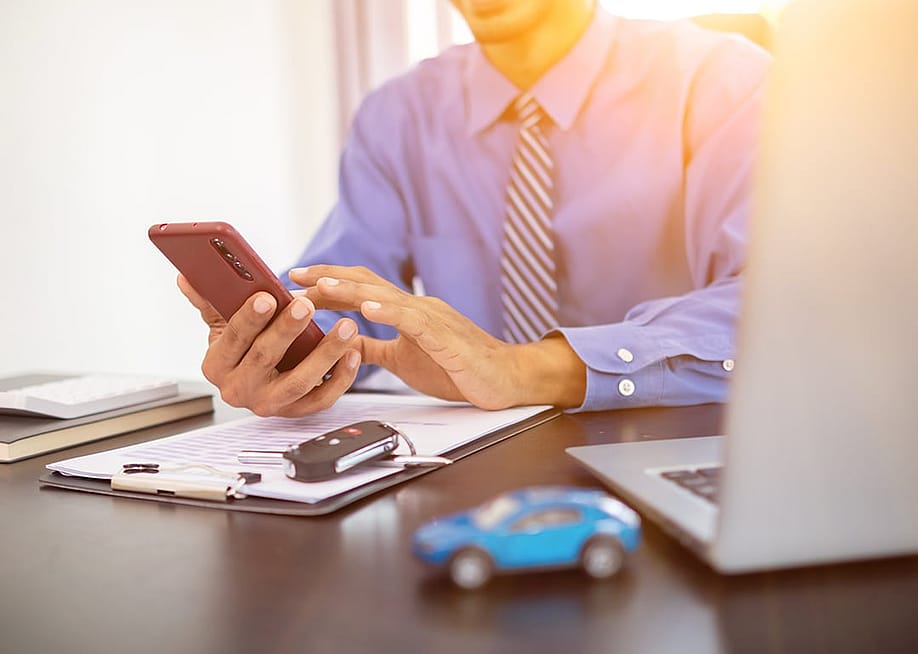 A car dealer calculating monthly car payments for customers from a smartphone. — Korawat photo shoot // Shutterstock