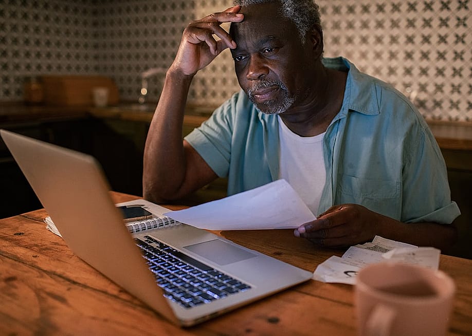 An elderly man reviewing his budget and finances from a laptop at home. — Geber86 // Shutterstock