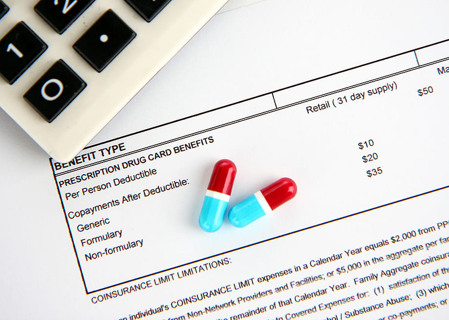 Two medicine pills and a calculator placed above a medical statement. — Rob Marmion // Shutterstock
