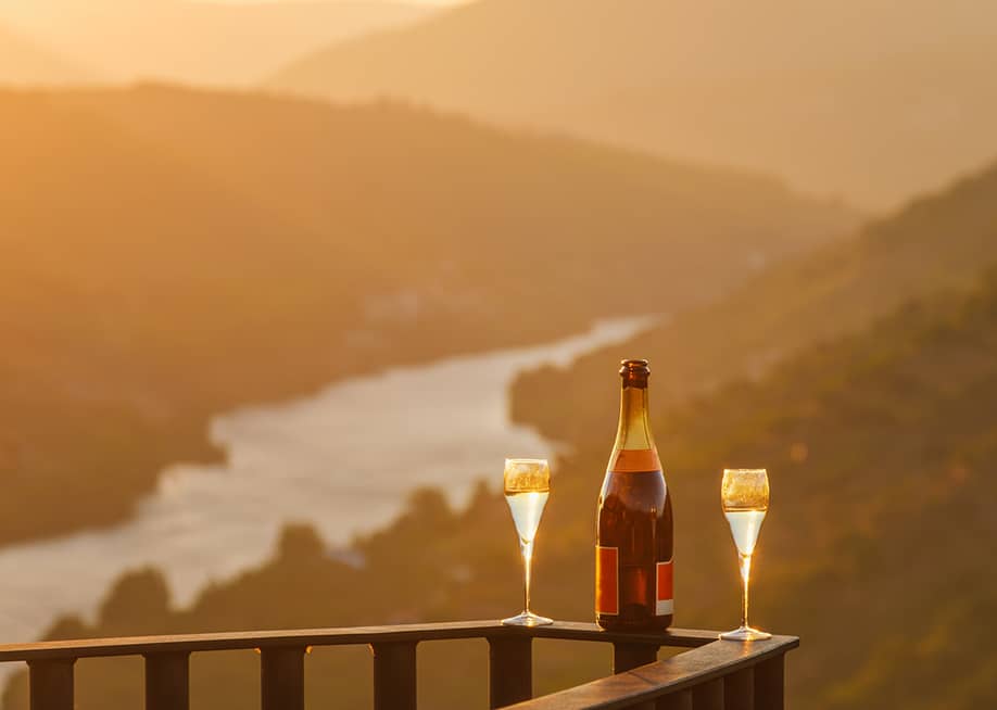 A bottle of wine and two glasses on a balcony rail with the view of the Douro Valley in Portugal. — Dmitry Rukhlenko // Shutterstock