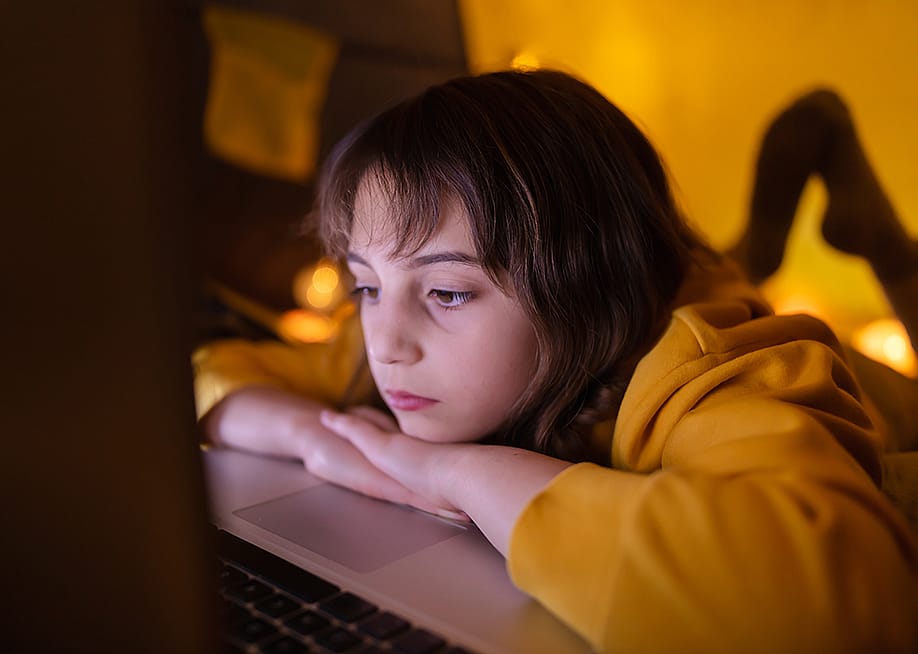 A young girl using her laptop inside a made-up tent in her room. — AstroStar // Shutterstock