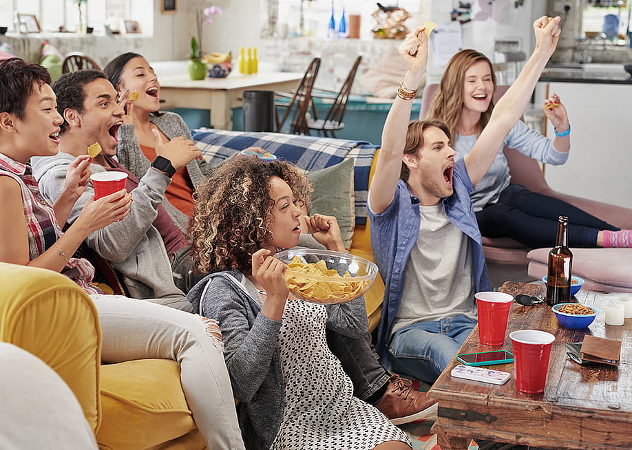 A group of friends celebrating at home while watching a soccer match. — PeopleImages // Shutterstock