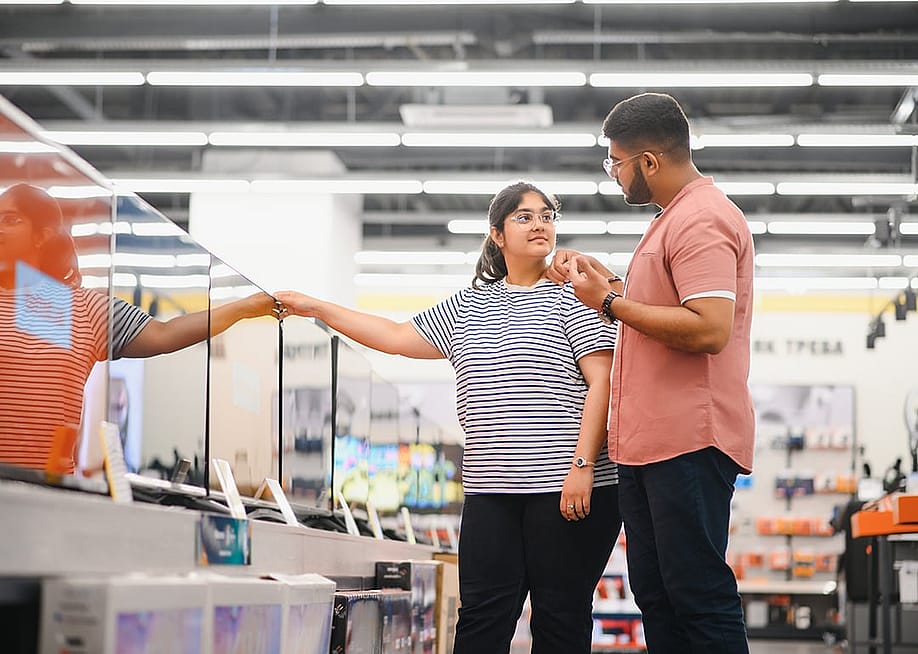 A young couple at an appliance store contemplating to buy a new flatscreen TV. — Hryshchyshen Serhii // Shutterstock