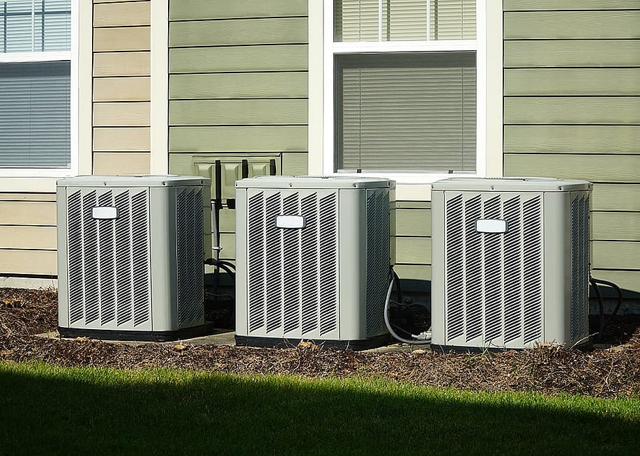 Three air conditioner compressor units placed behind a house. — ND700 // Shutterstock