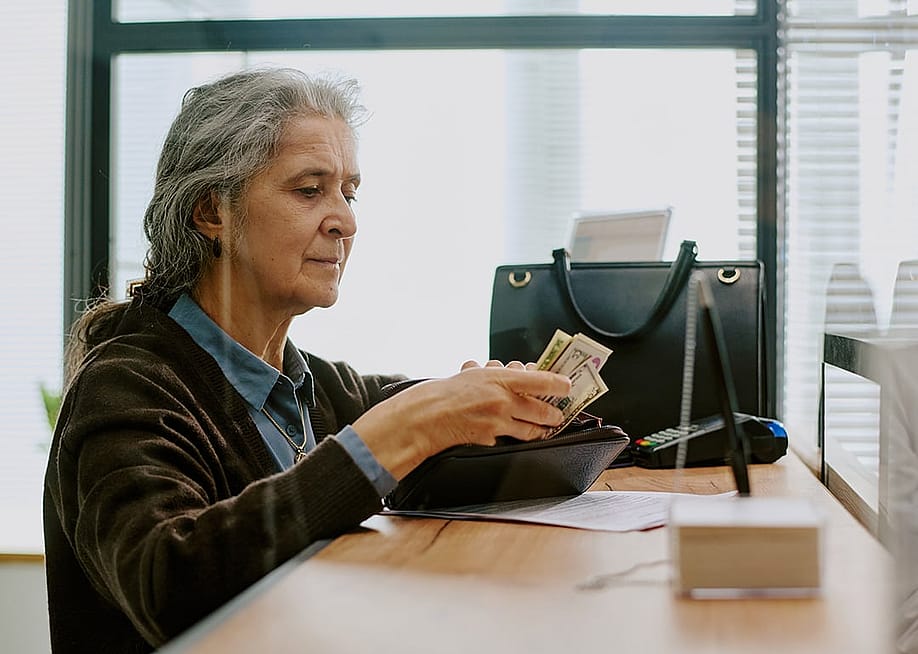 An elderly person preparing cash for a deposit transaction in a bank. — AnnaStills // Shutterstock
