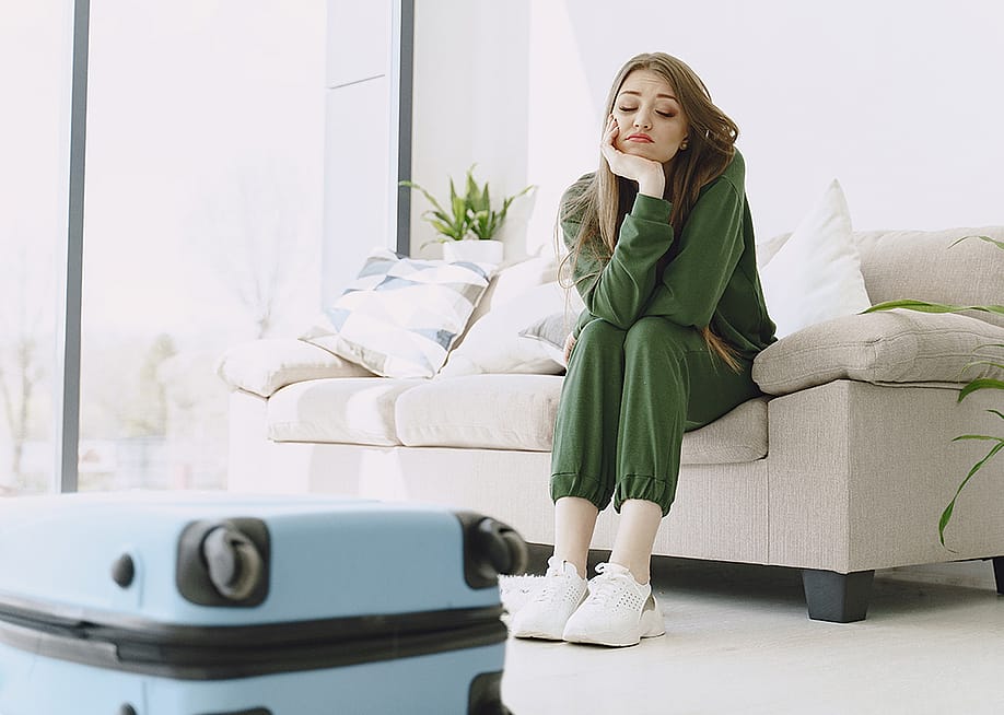 A young woman feeling sad after unpacking luggage from a trip. — Oleggg // Shutterstock