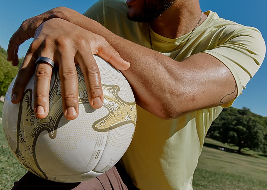 A person wearing a smart sleep ring while holding a ball outdoors. — Oura