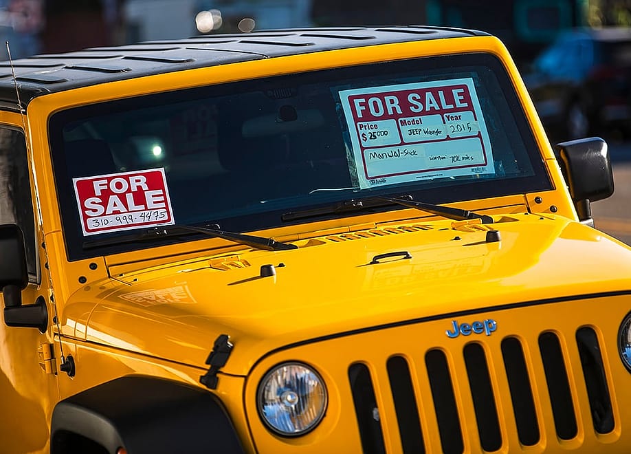 A yellow Jeep Wrangler for sale, with labels also put in the windows. — Karolis Kavolelis // Shutterstock