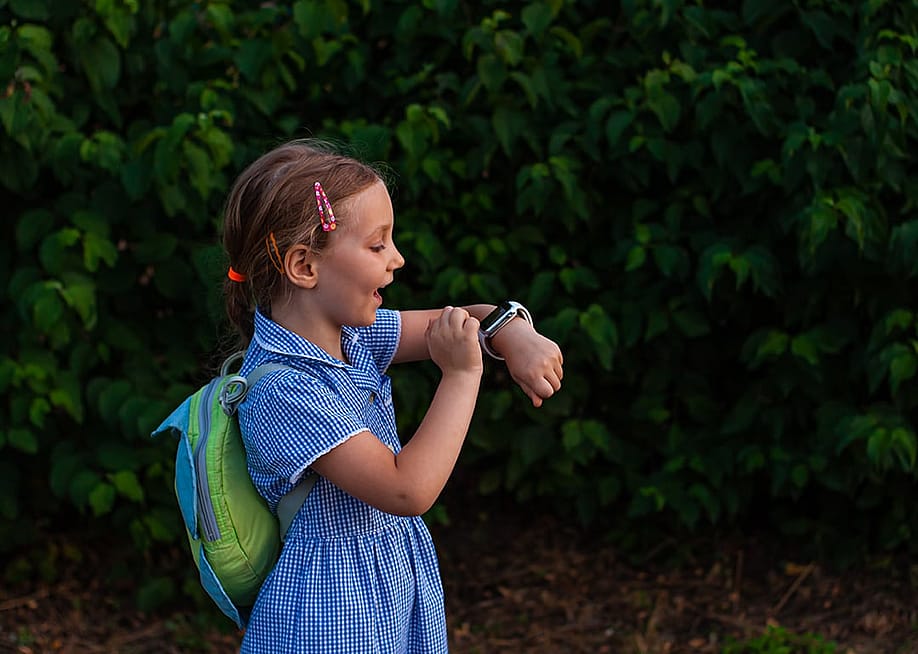 A school kid using her smartwatch outdoors in a park. — KawaiiS // Shutterstock