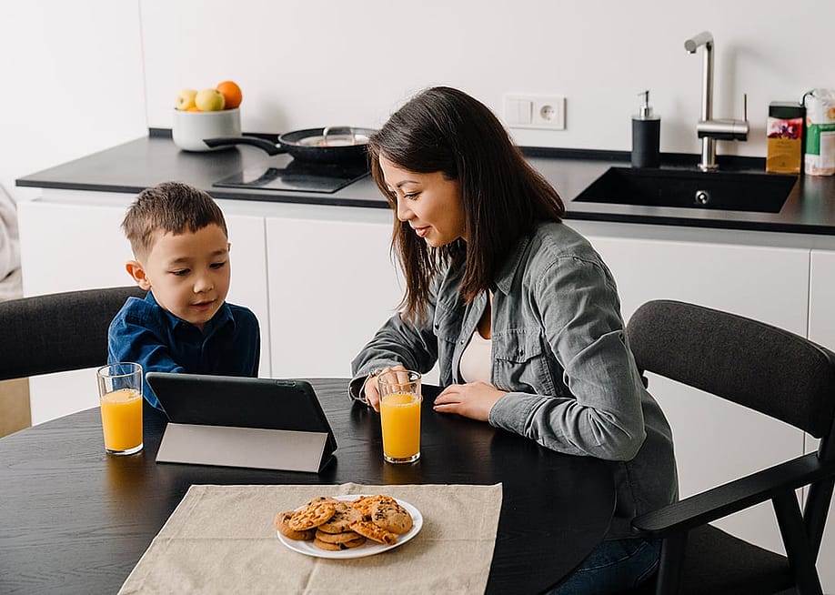 A mother with her young son watching something together on a tablet while having breakfast at home. — Dean Drobot // Shutterstock