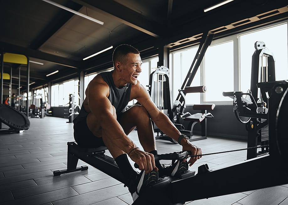 A cheerful man working out using a rowing gym equipment. — Davidovici // Shutterstock