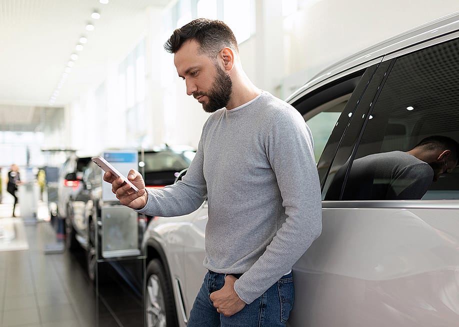 A man at a car dealership looking at information on his phone. — Jasen Wright // Shutterstock