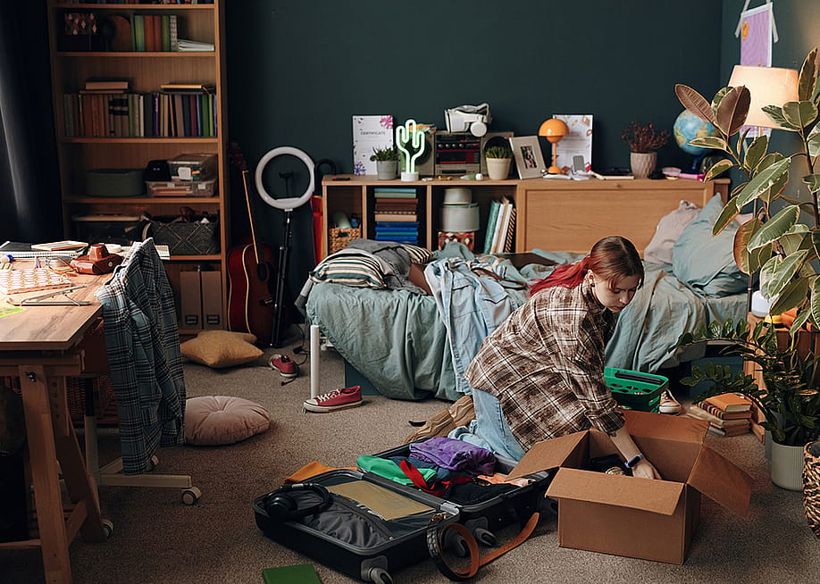 A young woman packing her items into a box in her bedroom. — Dragon Images // Shutterstock