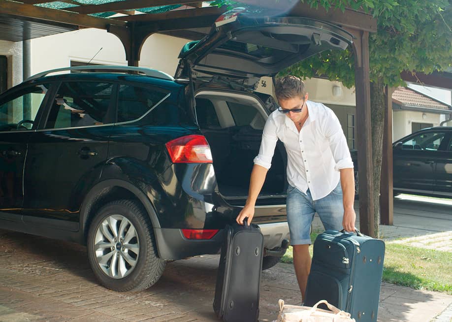 Man unloading heavy suitcases from his SUV's trunk. — Flystock // Shutterstock