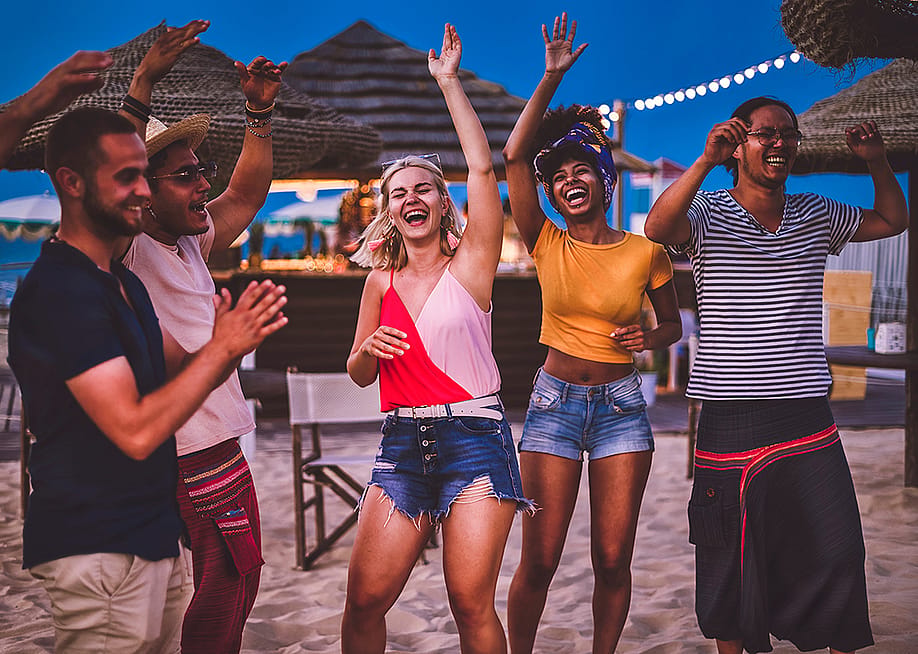 A group of friends dancing happily during a sunset party in the beach. — charmedlightph // Shutterstock