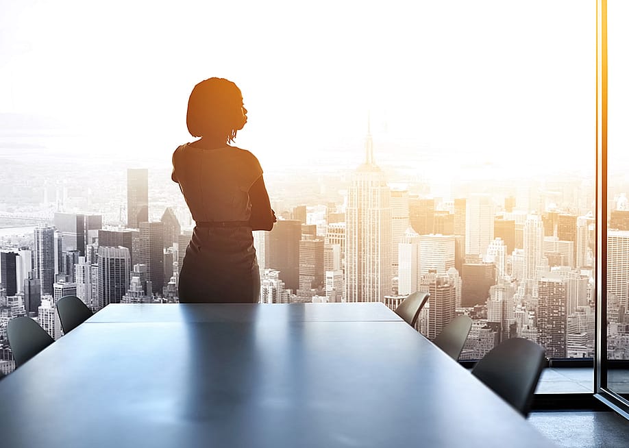 Rearview shot of a young businesswoman looking out from a large window in the office. — PeopleImages // Shutterstock