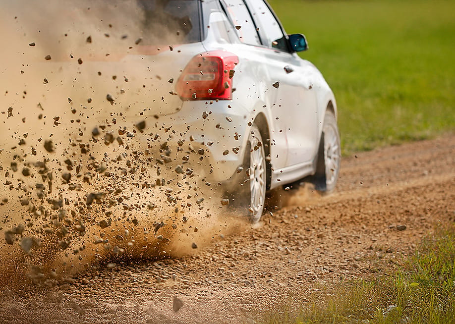 Gravel splashing from the wheels of a race car drifting on track. — Toa55 // Shutterstock