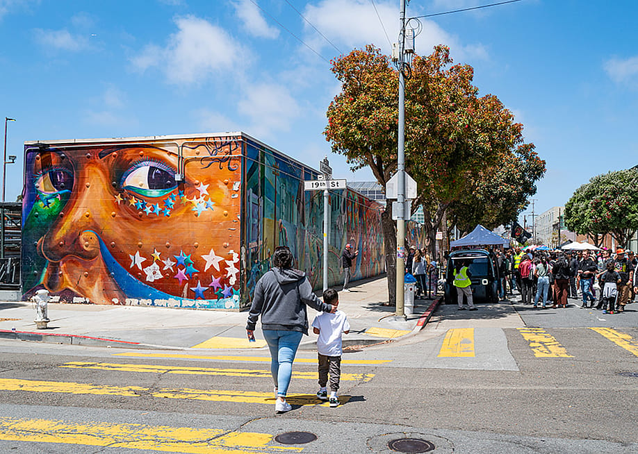 A mother and a child crossing the street near a mural at the other side. — Chris Allan // Shutterstock