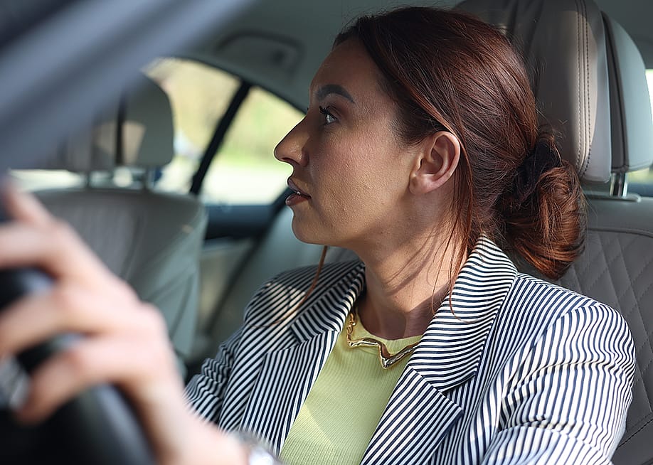 An office employee looking at her car's rear view mirror during parking. — Iaroslavv // Shutterstock
