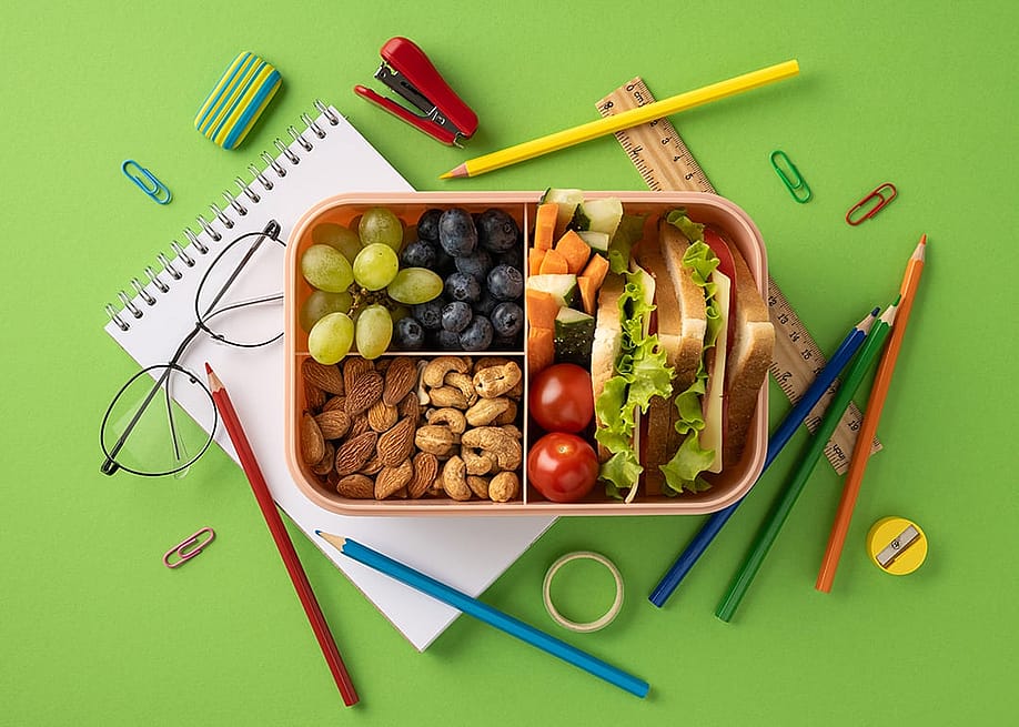 A lunchbox packed with a variety of healthy snacks surrounded by school supplies. — Inspiration GP // Shutterstock