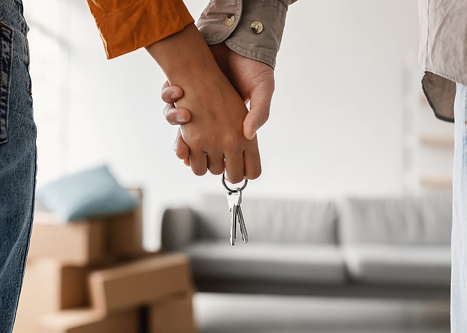 A closeup shot of a young couple holding hands with a house key of their new house. — Prostock-studio // Shutterstock