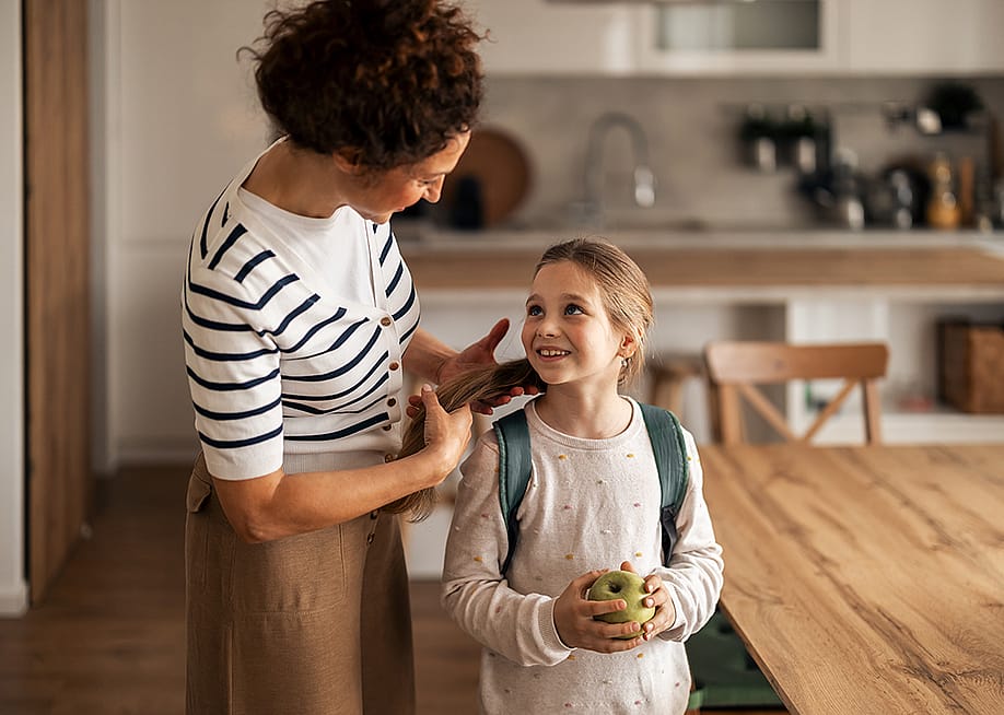 A mother preparing her young daughter to go to school. — Jelena Zelen // Shutterstock