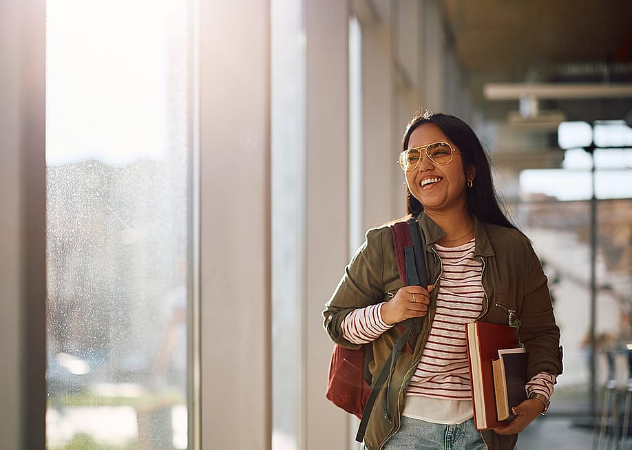 A smiling university student standing in the campus' hallway before her classes start. — Drazen Zigic // Shutterstock