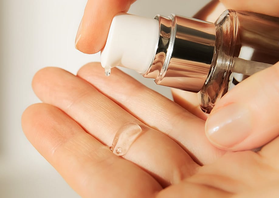 A cosmetologist squeezing out a moisturizing hyaluronic serum on her hand before a facial session. — AliceCam // Shutterstock