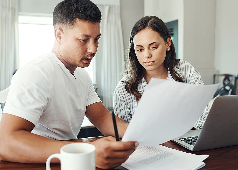 A married couple reviewing their family's financial documents and other paperwork for a loan refinancing. — PeopleImages // Shutterstock