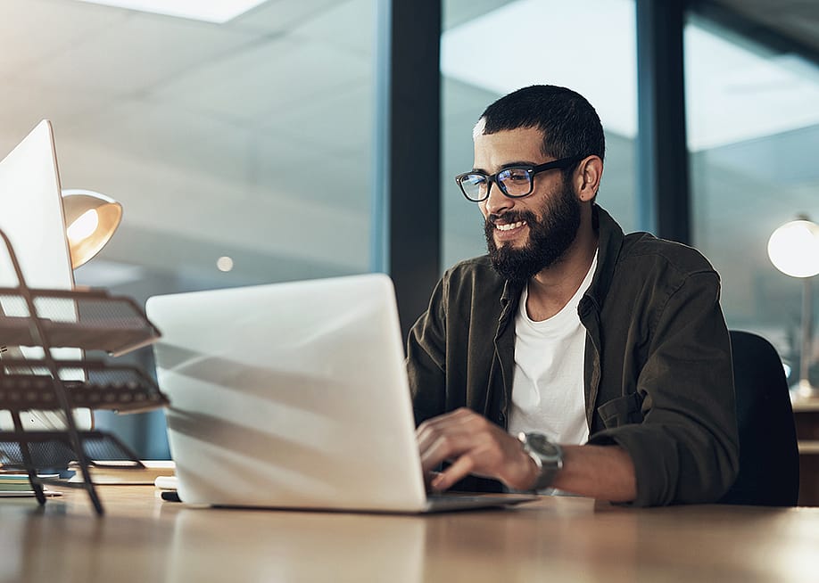 A young businessman happily communicating in the office using a laptop. — PeopleImages // Shutterstock