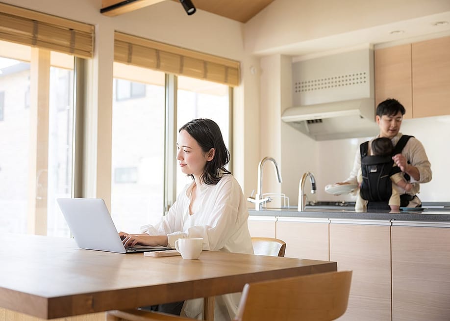 Young parents where the mother works remotely from their home kitchen and the father takes care of their infant child. — kapinon.studio // Shutterstock