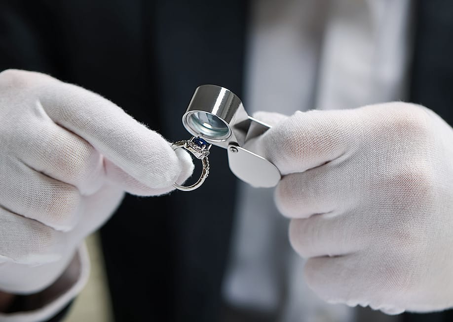 An appraiser evaluating a blue sapphire and diamond ring with a loupe. — New Africa // Shutterstock