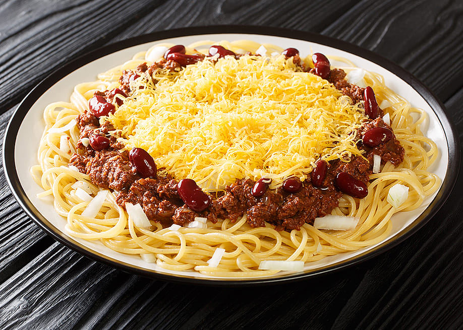 A Cincinnati chili spaghetti with meat, beans, onions, and cheese served in a plate. — Sergii Koval // Shutterstock